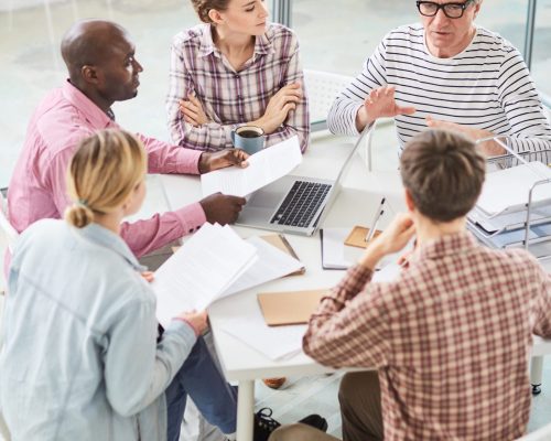 Group of contemporary office workers sitting in circle during start-up meeting and listening to speaker